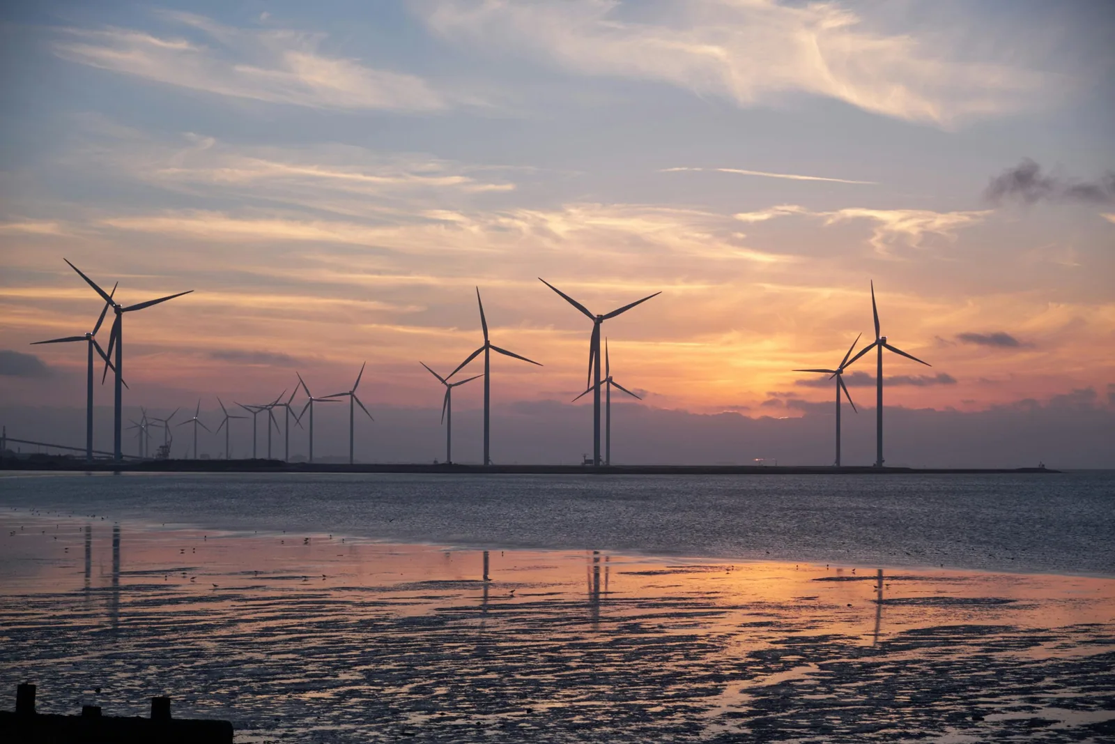 Tall windmills on a coastal wind farm at sunset.